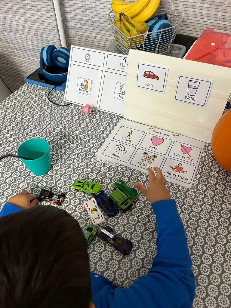A child playing with toy cars beside core-word symbols and a now-and-next board